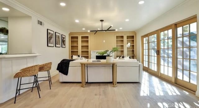 living room featuring light wood-type flooring, french doors, crown molding, and a chandelier