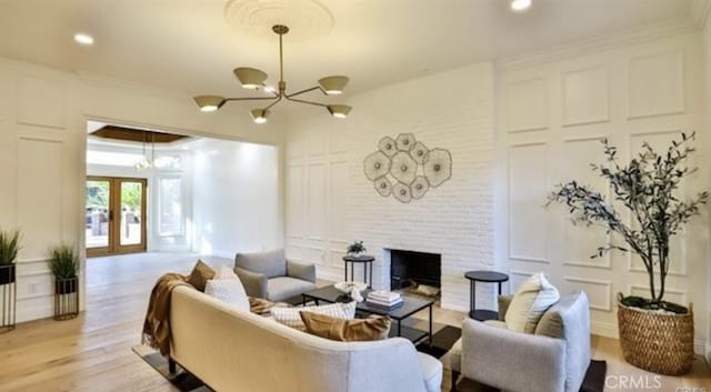 living room with french doors, an inviting chandelier, a fireplace, ornamental molding, and light hardwood / wood-style flooring