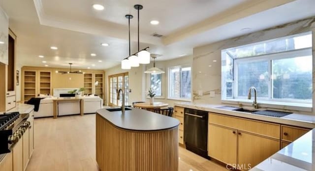 kitchen with dishwasher, pendant lighting, sink, a tray ceiling, and an island with sink