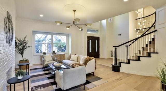 living room with a brick fireplace, crown molding, light hardwood / wood-style flooring, and a notable chandelier