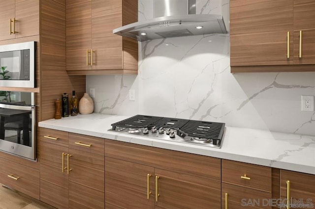 kitchen with light stone counters, island exhaust hood, stainless steel appliances, and backsplash