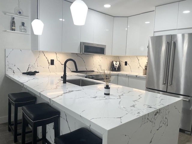 kitchen with light stone countertops, appliances with stainless steel finishes, decorative light fixtures, white cabinetry, and sink