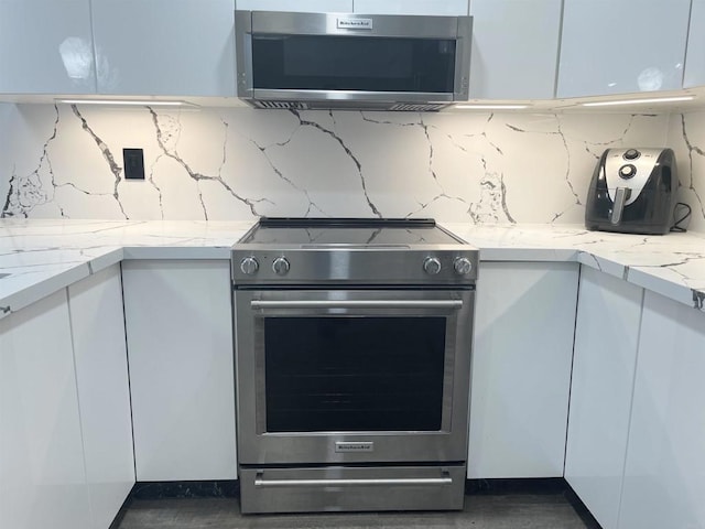 kitchen with stainless steel appliances, backsplash, white cabinets, and light stone countertops