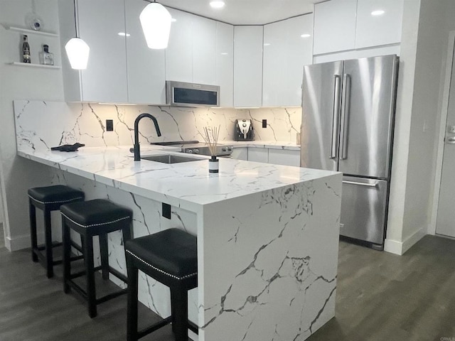 kitchen featuring pendant lighting, white cabinetry, kitchen peninsula, stainless steel appliances, and dark wood-type flooring