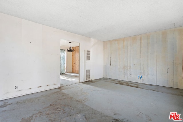 empty room with a notable chandelier, wooden walls, and concrete floors