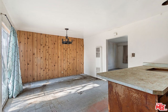 unfurnished dining area with a notable chandelier and wooden walls