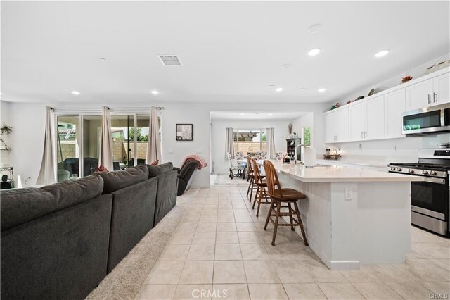 kitchen with light tile patterned floors, white cabinetry, appliances with stainless steel finishes, a kitchen island with sink, and a kitchen breakfast bar