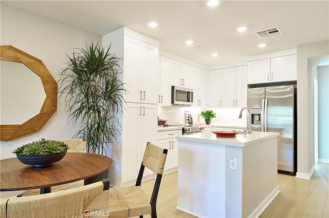 kitchen featuring a center island with sink, sink, white cabinetry, light hardwood / wood-style flooring, and stainless steel appliances