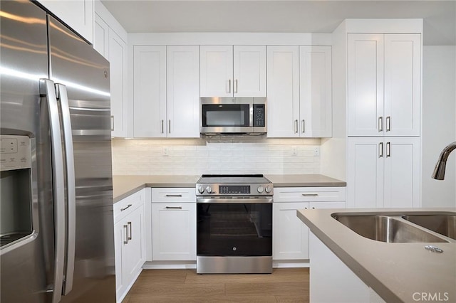 kitchen featuring sink, white cabinetry, hardwood / wood-style flooring, stainless steel appliances, and backsplash