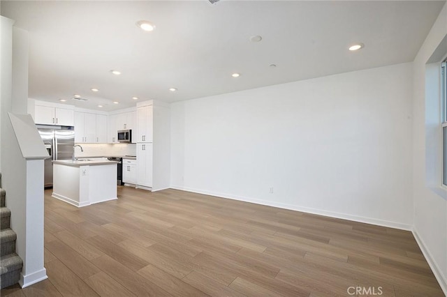 kitchen featuring sink, white cabinetry, stainless steel appliances, a center island with sink, and light wood-type flooring