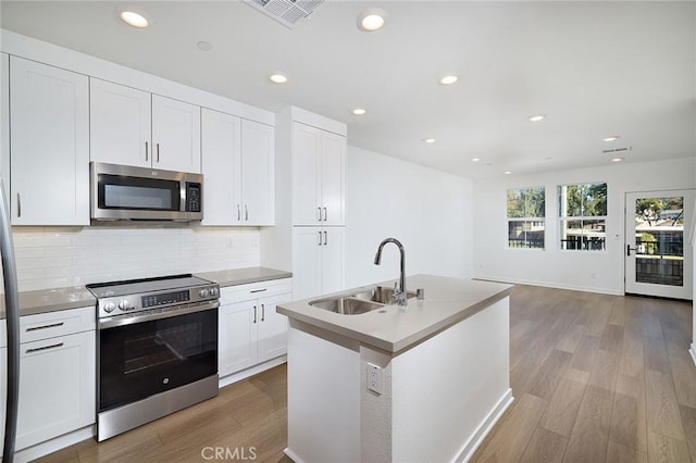 kitchen featuring hardwood / wood-style floors, sink, white cabinets, a kitchen island with sink, and stainless steel appliances