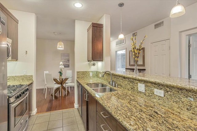 kitchen with sink, hanging light fixtures, light tile patterned floors, appliances with stainless steel finishes, and light stone countertops