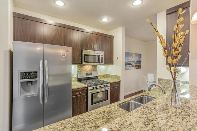 kitchen featuring stainless steel appliances, light stone countertops, sink, and dark brown cabinets