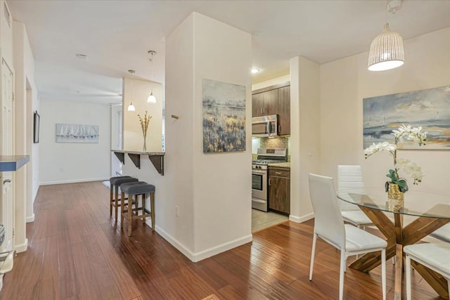 kitchen featuring appliances with stainless steel finishes, a breakfast bar, hardwood / wood-style floors, and dark brown cabinetry