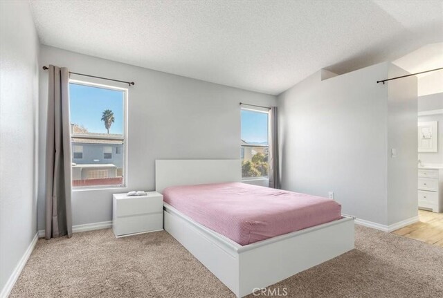 bedroom featuring ensuite bathroom, light carpet, and a textured ceiling