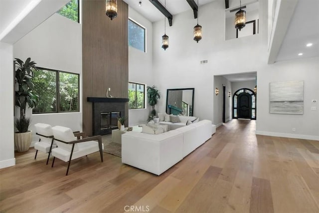 living room featuring beam ceiling, a healthy amount of sunlight, a large fireplace, and light hardwood / wood-style flooring