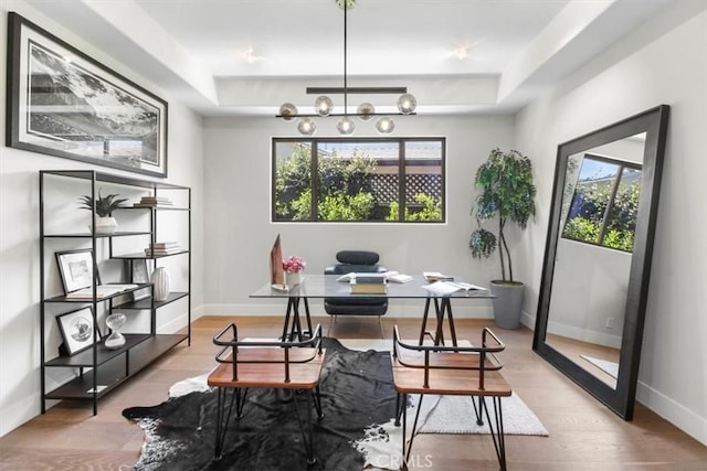 dining room with a wealth of natural light, light hardwood / wood-style floors, a raised ceiling, and a notable chandelier