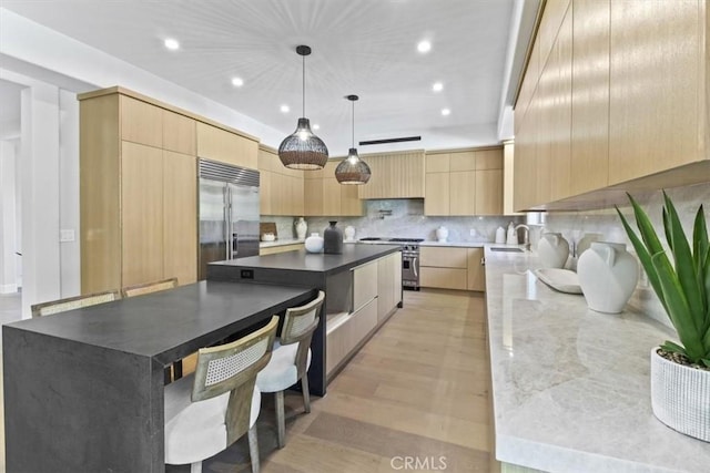 kitchen featuring a center island, decorative light fixtures, high end appliances, light brown cabinetry, and backsplash