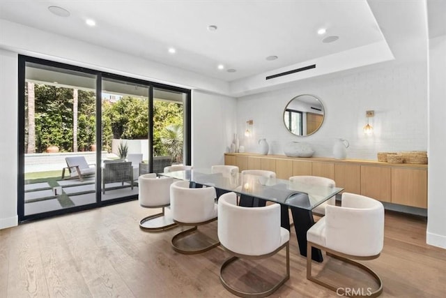 dining area with light hardwood / wood-style floors and a tray ceiling