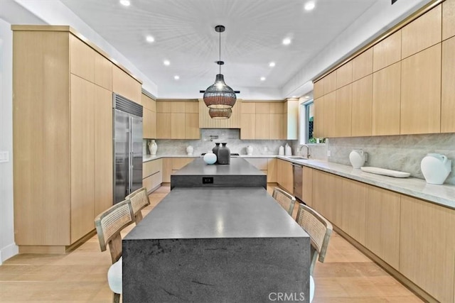 kitchen with stainless steel appliances, light brown cabinetry, light hardwood / wood-style flooring, and decorative light fixtures