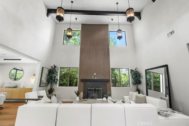 living room featuring a healthy amount of sunlight, wood-type flooring, a large fireplace, and beamed ceiling