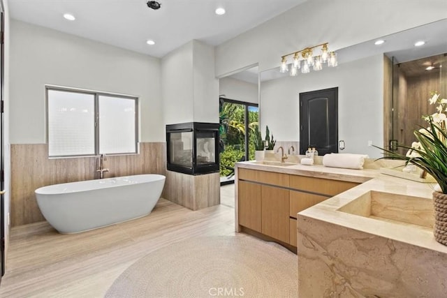 bathroom featuring vanity, a multi sided fireplace, and a tub