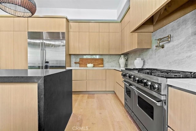 kitchen featuring light wood-type flooring, light brown cabinetry, premium appliances, and tasteful backsplash