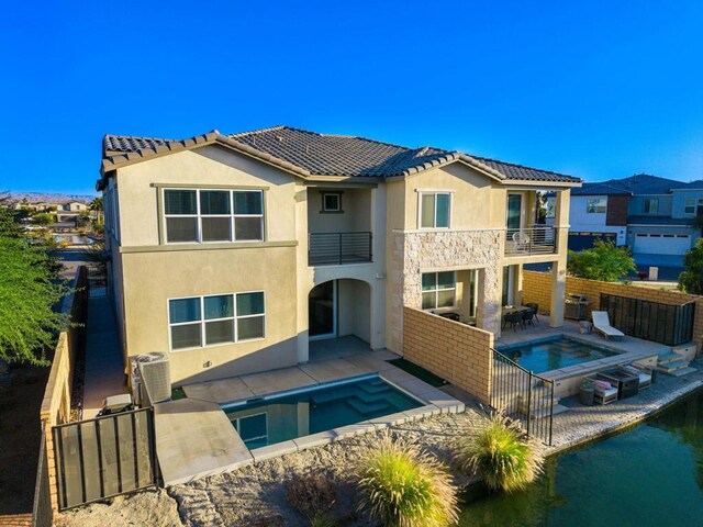 back of property with central AC unit, a swimming pool with hot tub, a balcony, and a patio