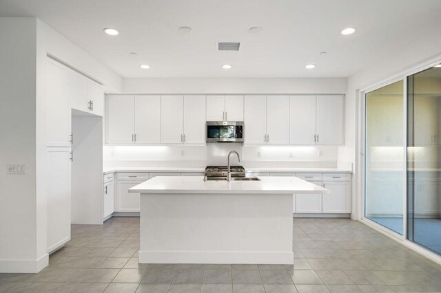 kitchen featuring sink, white cabinetry, light tile patterned floors, and an island with sink