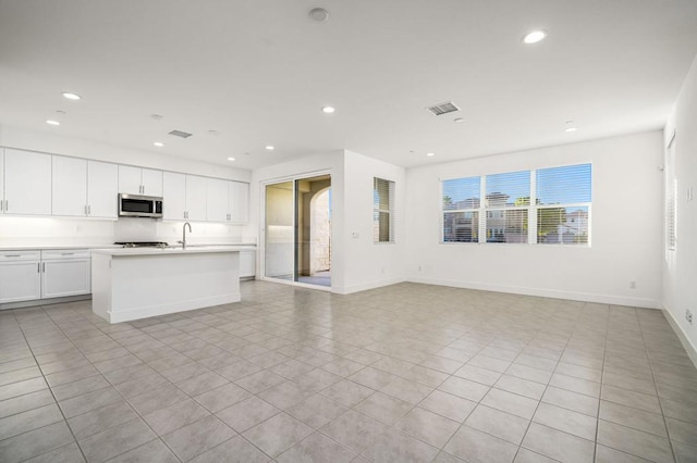 kitchen with sink, white cabinetry, light tile patterned floors, and a center island with sink