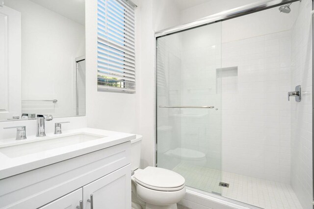 bathroom featuring toilet, a shower with shower door, and vanity