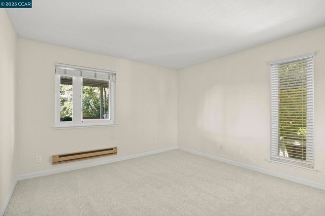 unfurnished room featuring baseboard heating, light colored carpet, and plenty of natural light