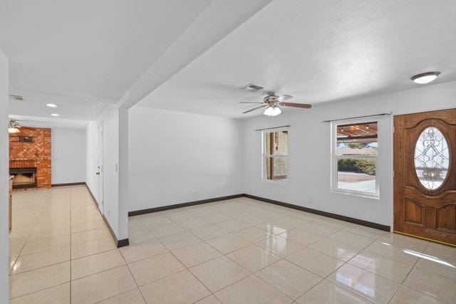 tiled foyer entrance with ceiling fan and a brick fireplace