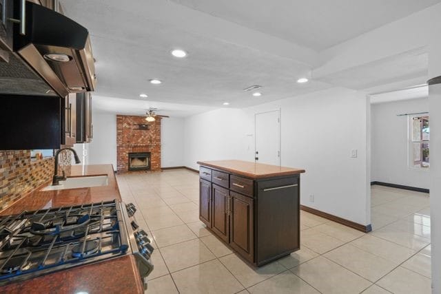 kitchen with a center island, a fireplace, sink, stainless steel gas cooktop, and ceiling fan