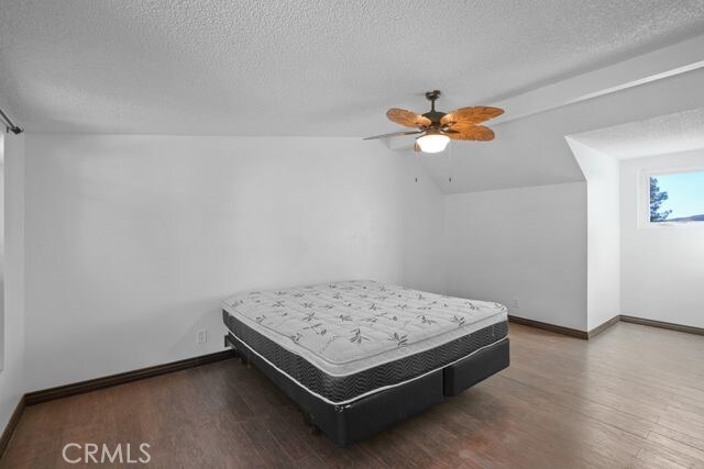 bedroom with vaulted ceiling, ceiling fan, a textured ceiling, and dark hardwood / wood-style floors