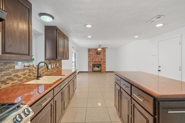 kitchen with tasteful backsplash, ceiling fan, sink, a brick fireplace, and light tile patterned floors