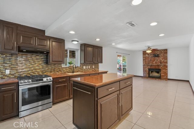 kitchen with stainless steel gas range oven, a brick fireplace, ceiling fan, tasteful backsplash, and sink