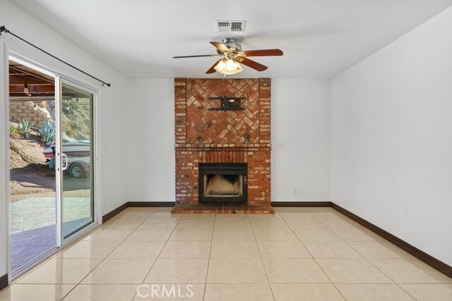 unfurnished living room featuring ceiling fan, light tile patterned floors, and a brick fireplace