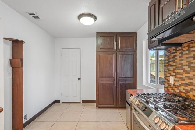 kitchen with dark brown cabinets, light tile patterned flooring, stainless steel stove, and decorative backsplash