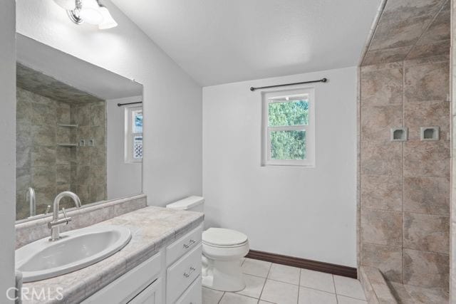 bathroom featuring toilet, tile patterned flooring, tiled shower, and vanity