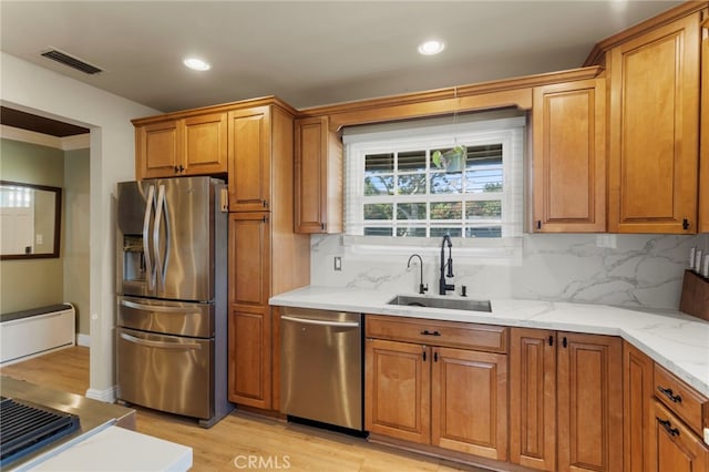 kitchen with light hardwood / wood-style floors, stainless steel appliances, decorative backsplash, light stone counters, and sink