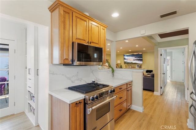 kitchen featuring appliances with stainless steel finishes, decorative backsplash, light hardwood / wood-style floors, kitchen peninsula, and light stone counters