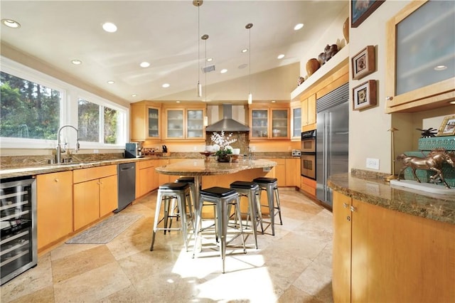 kitchen with decorative light fixtures, beverage cooler, light stone countertops, vaulted ceiling, and wall chimney range hood