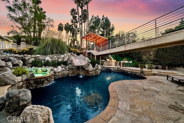 pool at dusk with pool water feature, an in ground hot tub, and a patio area