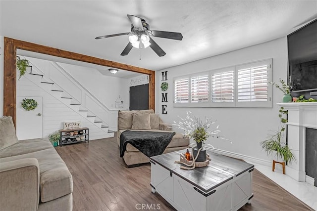 living room with ceiling fan, hardwood / wood-style flooring, a premium fireplace, and beamed ceiling