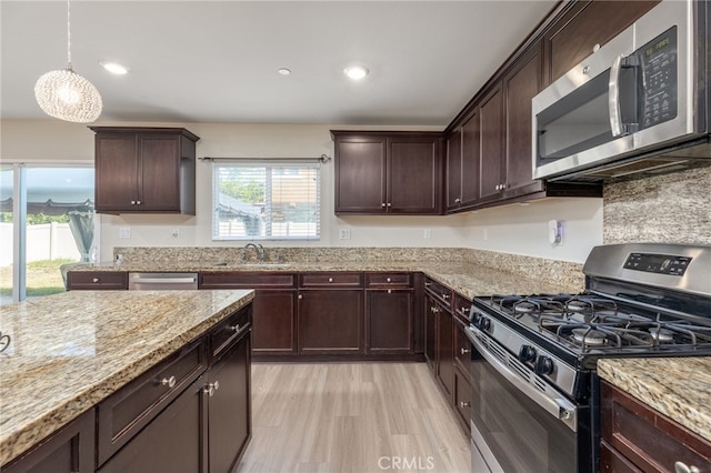 kitchen with pendant lighting, sink, stainless steel appliances, light stone counters, and light hardwood / wood-style floors