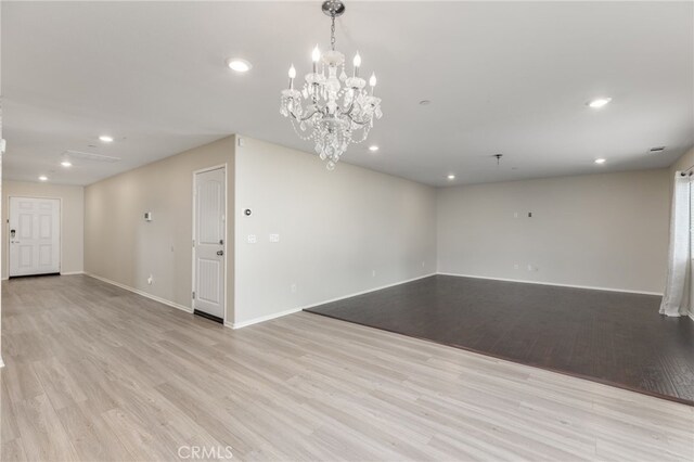 empty room featuring a notable chandelier and light wood-type flooring