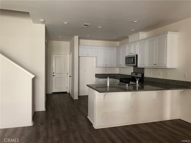 kitchen with dark hardwood / wood-style floors, kitchen peninsula, appliances with stainless steel finishes, a kitchen breakfast bar, and white cabinets