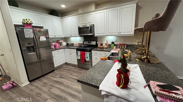 kitchen with white cabinetry, kitchen peninsula, stainless steel appliances, light hardwood / wood-style flooring, and sink