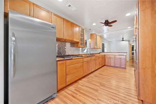 kitchen featuring appliances with stainless steel finishes, light brown cabinetry, backsplash, ceiling fan, and light hardwood / wood-style flooring